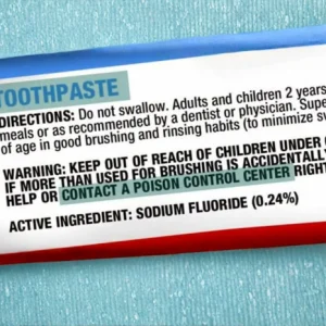 Close-up image of a fluoride toothpaste package displaying sodium fluoride (0.24%) as the active ingredient and a Poison Control warning if swallowed. Educational visual discussing fluoride toothpaste ingredients, oral health safety, consumer awareness, and toothpaste warning labels.